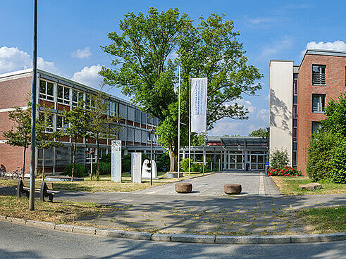 Panoramaaufnahme eines modernen, mehrstöckigen Backsteingebäudes unter blauem Himmel mit lockerer Bewölkung.